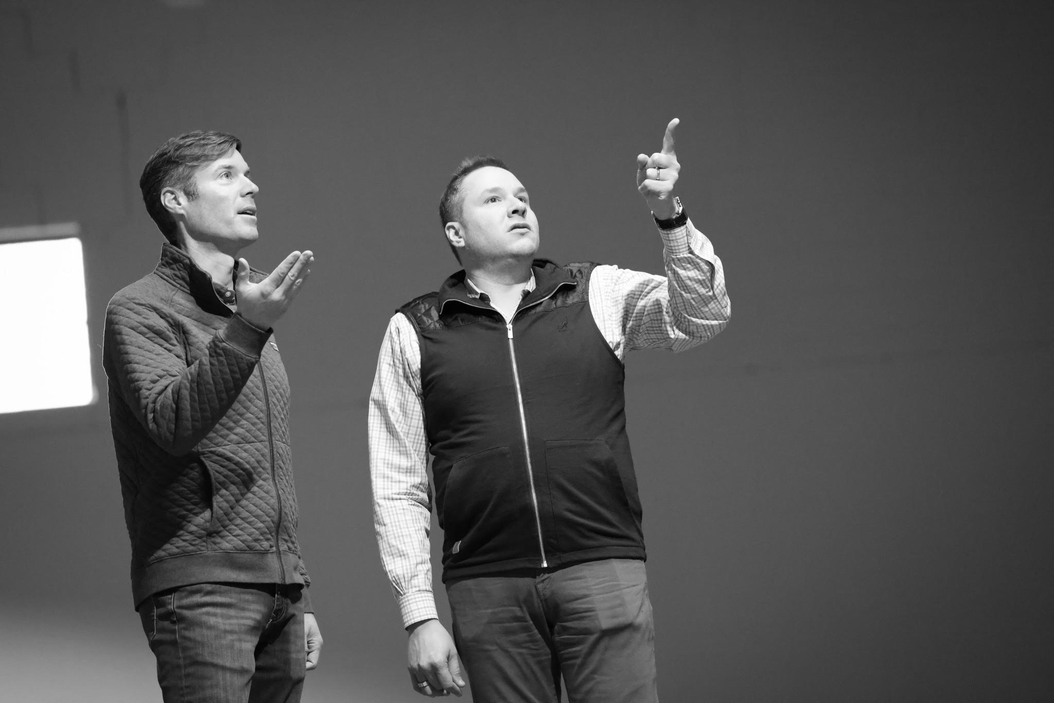 Monochrome photo of Ryan Gorman and Brian Iammartino on a worksite, pointing up at something out of frame